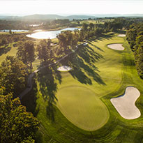 Aerial view of green golf course with sun and mountains.