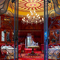 Delicately crafted iron gates opening to a fine-dining restaurant with deep red and gold. 