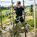 40' Ropes Course Man climbing through an elevated adventure ropes course on a sunny day.