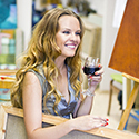 Art Classes Woman smiling with wine holding a painting canvas.
