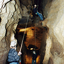 Person holding the rope of another climbing a cave wall.
